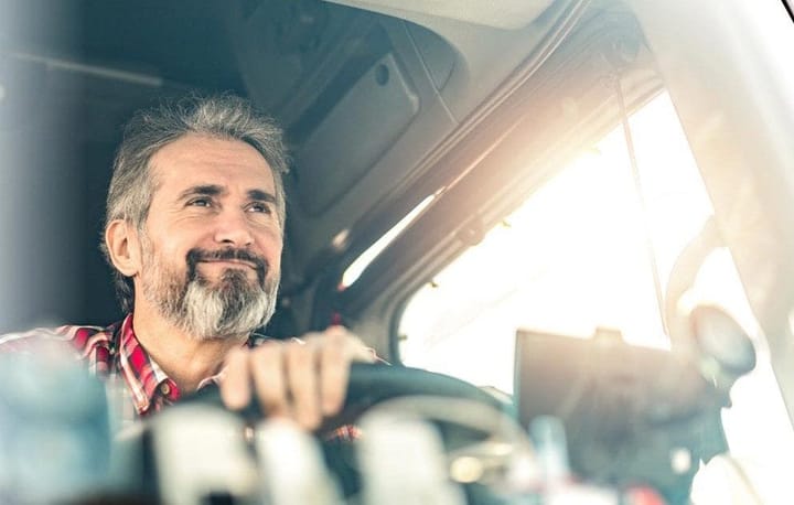 Fahrer eines Lkw lächelt zufrieden am Steuer, die Hand am Lenkrad